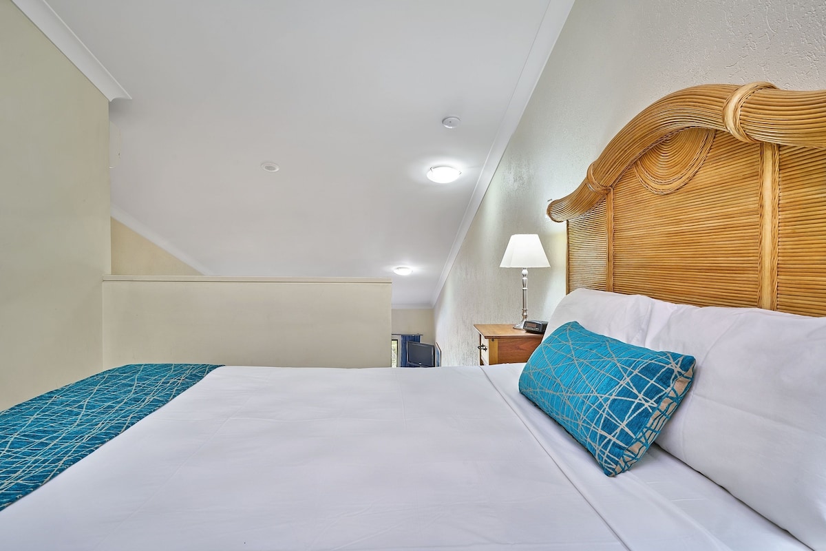 A hotel room with a bed, a nightstand, a lamp, and a wooden headboard.