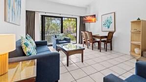 A living room with a sofa, coffee table, and dining area with chairs and a table. - Trinity Beach Club Holiday Apartments (Trinity Beach)