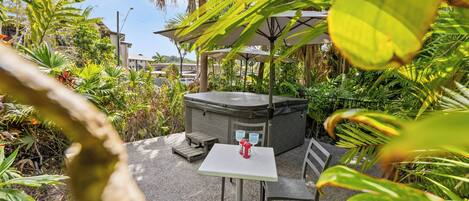 A hot tub with a table and chairs, surrounded by lush greenery and a clear sky.
