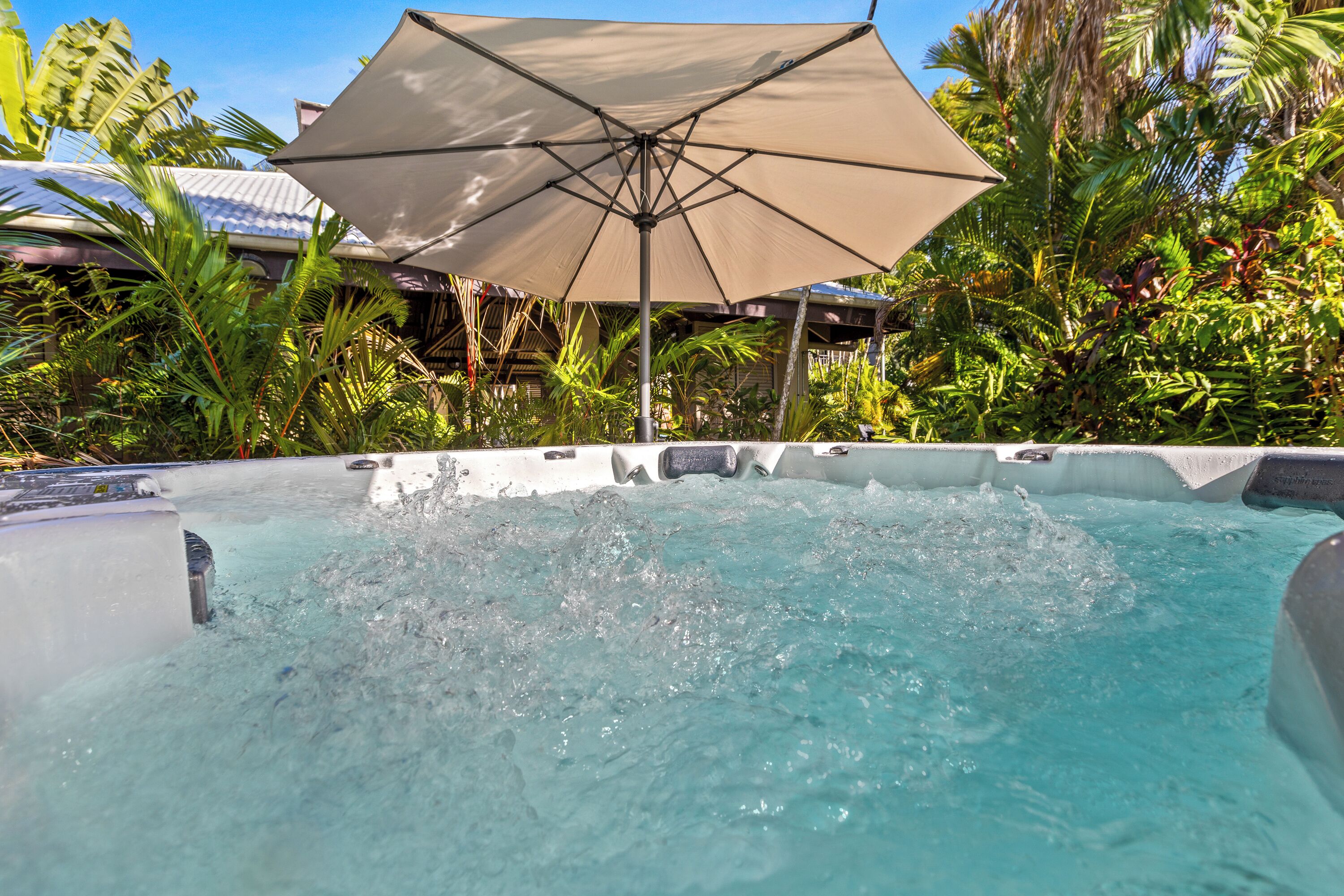 A hot tub with water splashing, surrounded by lush greenery and a large umbrella.