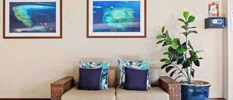 A wicker sofa with two cushions, a potted plant, and two framed pictures on the wall.
