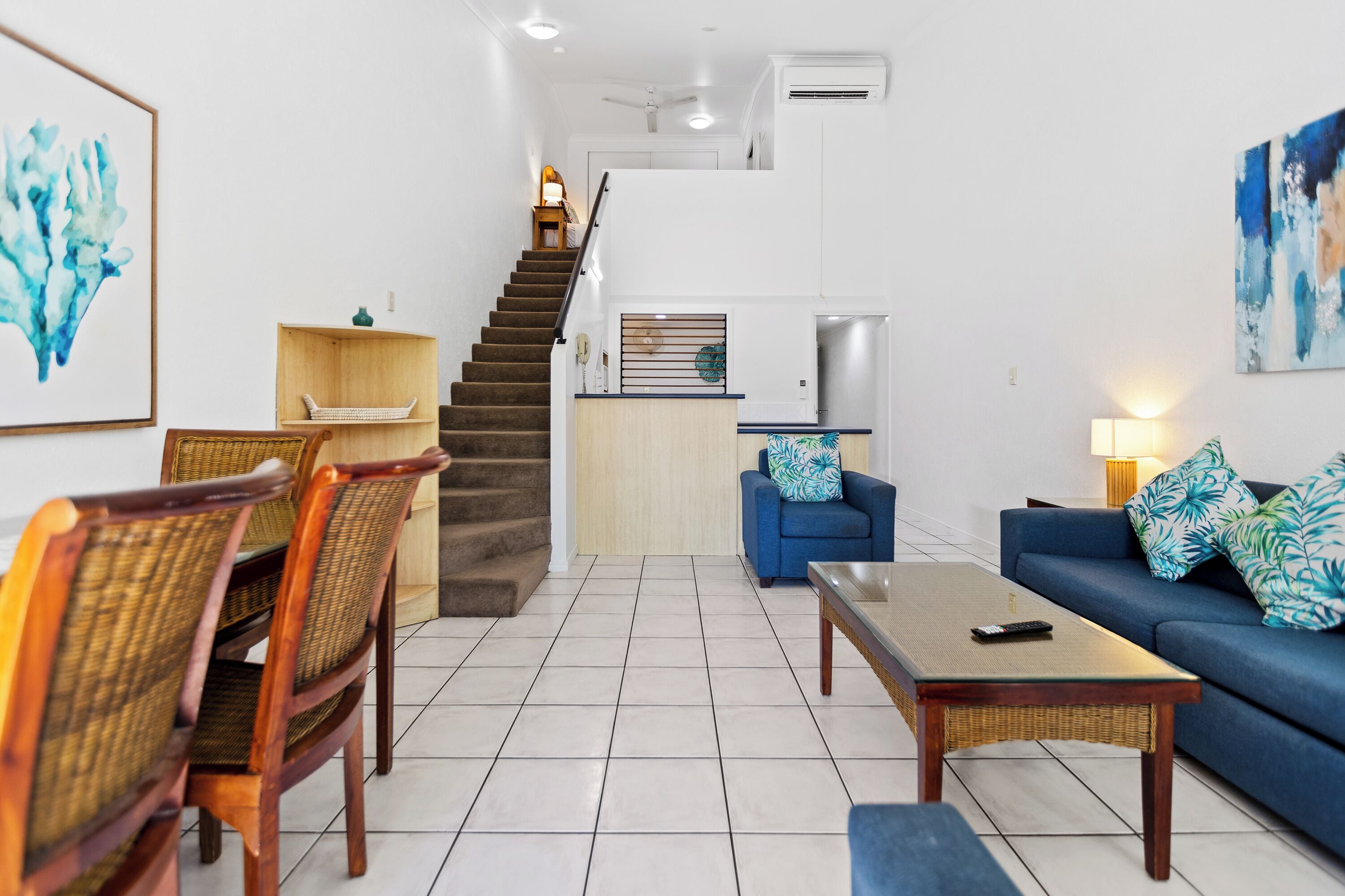 A modern living room with a staircase, a sofa, a coffee table, and a dining area with chairs.
