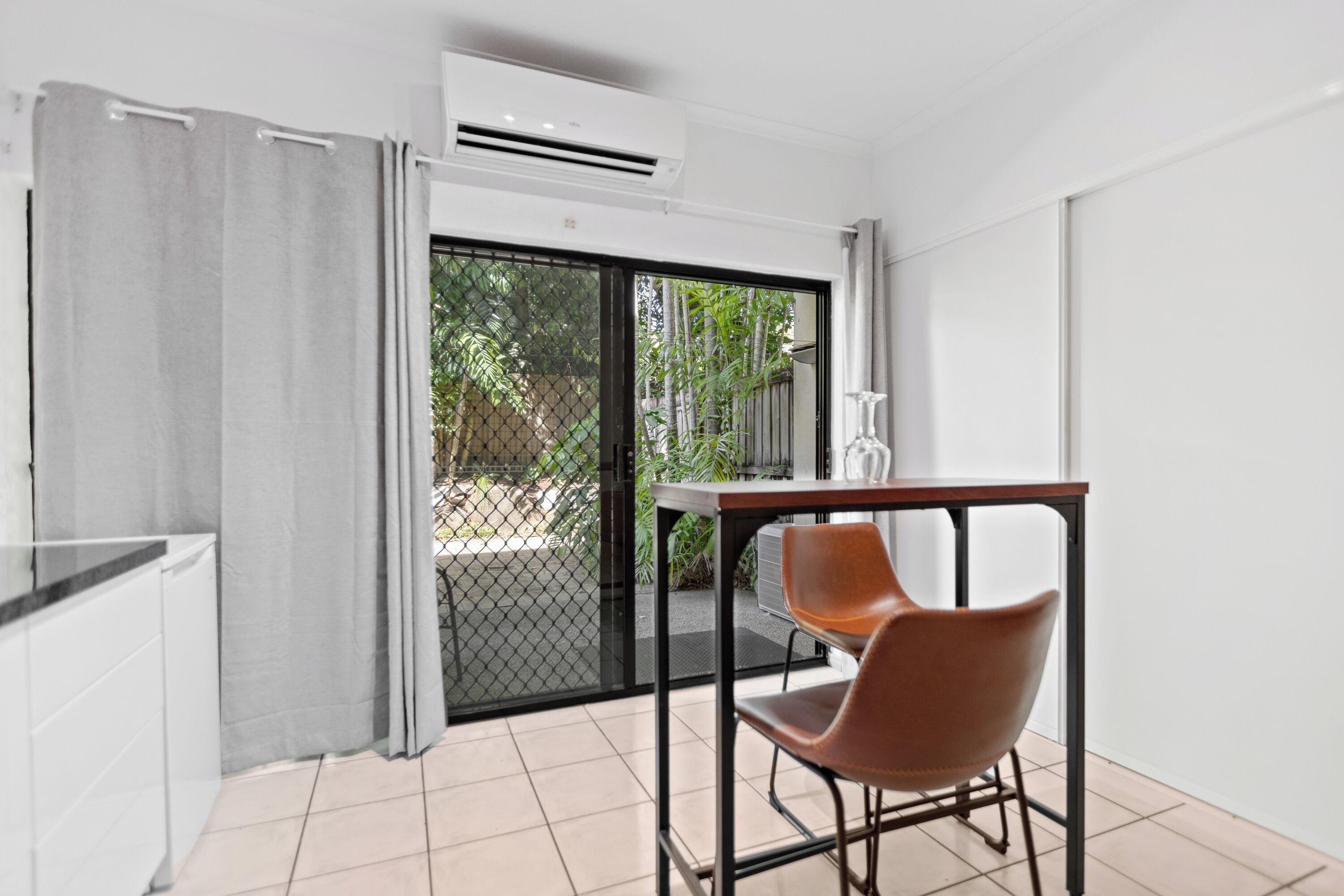 Une pièce comprenant une table et une chaise, un appareil de climatisation, une porte-fenêtre coulissante et une vue sur la verdure à l’extérieur.
