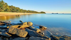 A beach with clear water, rocks, and palm trees. - Trinity Beach Club Holiday Apartments (Trinity Beach)