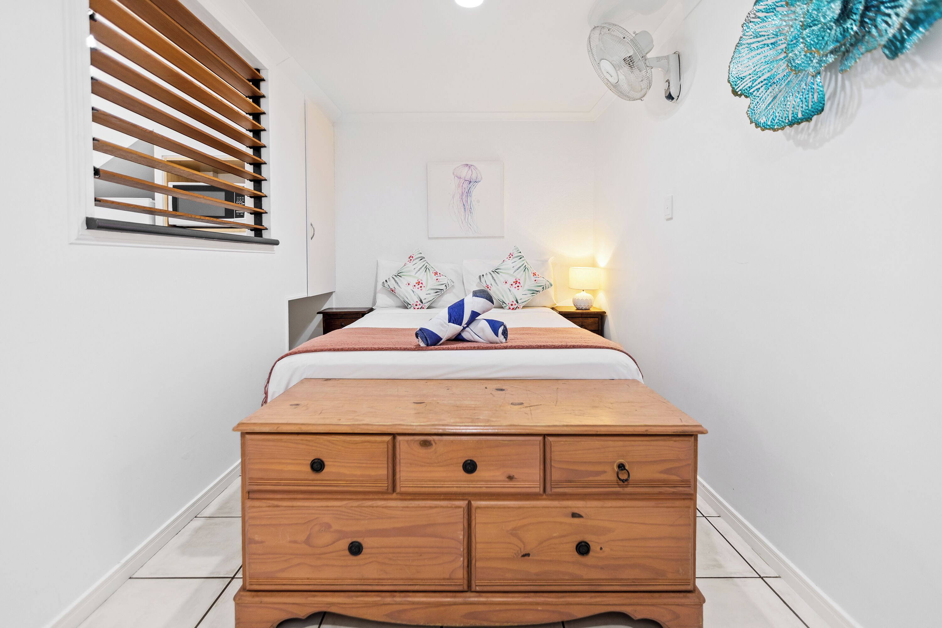 A bedroom with a wooden bed, a nightstand with a lamp, a wall clock, and a decorative wall hanging.
