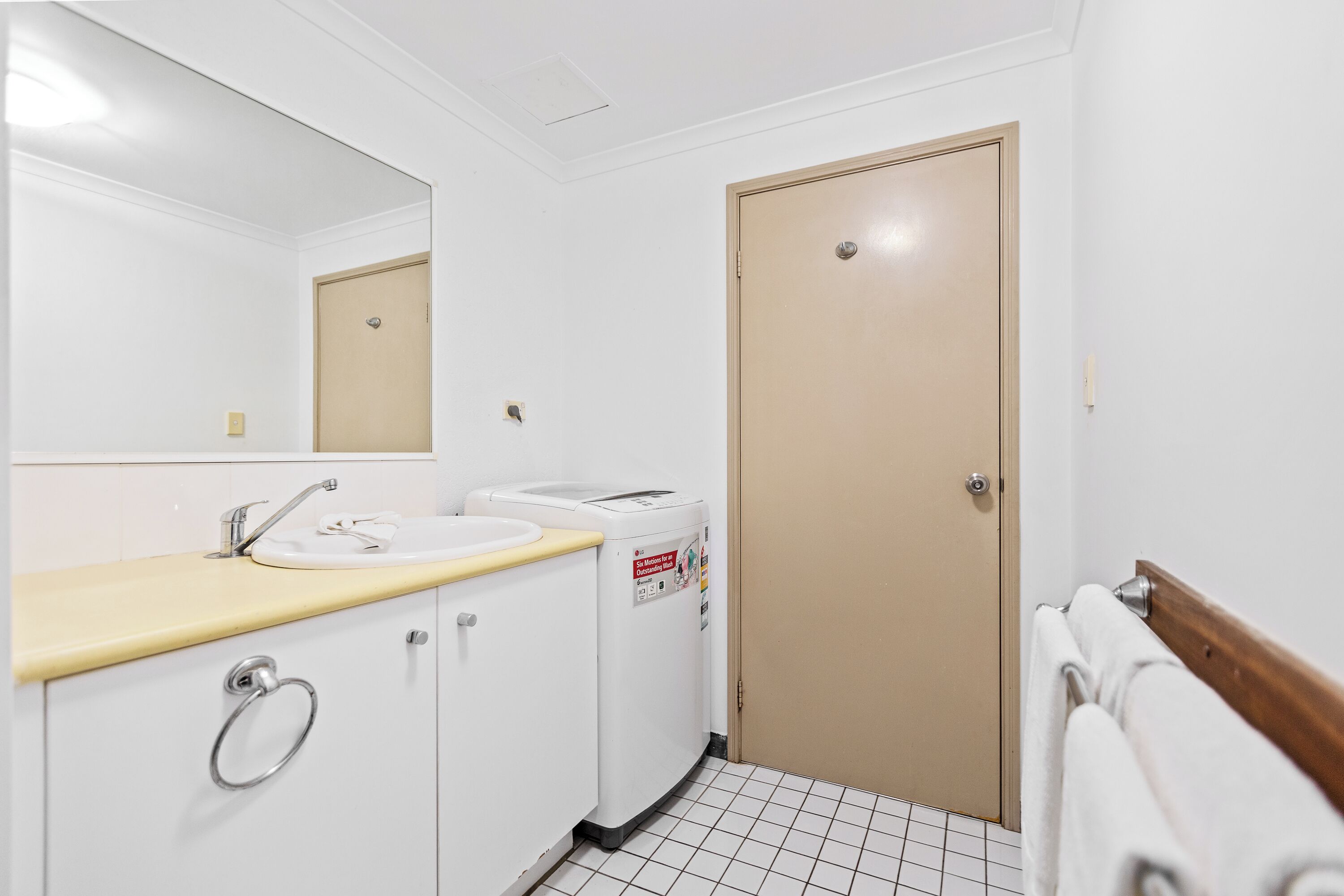 Une salle de bain avec un lavabo, un miroir, un porte-serviettes et une porte.