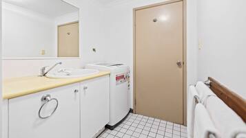 Un baño con lavamanos, espejo, perchero para toallas y una puerta.