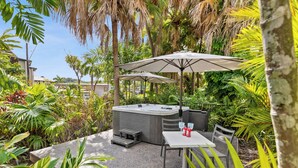 A hot tub surrounded by tropical plants, a table with chairs, and umbrellas. - Trinity Beach Club Holiday Apartments (Trinity Beach)
