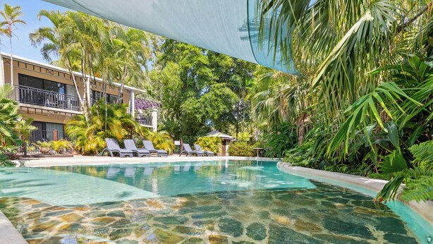 A swimming pool with clear water, surrounded by lush greenery and a building with balconies. - Trinity Beach Club Holiday Apartments (Trinity Beach)
