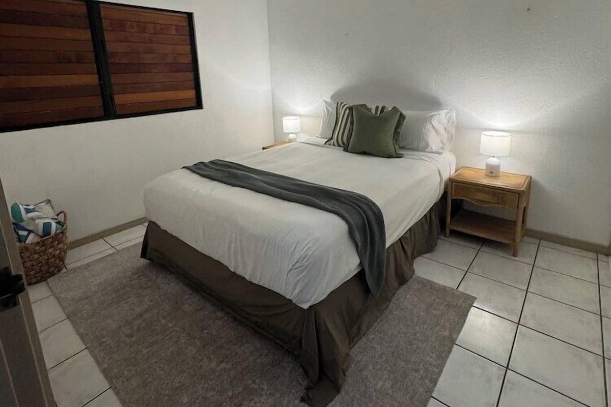 A bedroom with a bed, a nightstand, a ceiling fan, a wall-mounted shelf, and a tiled floor.