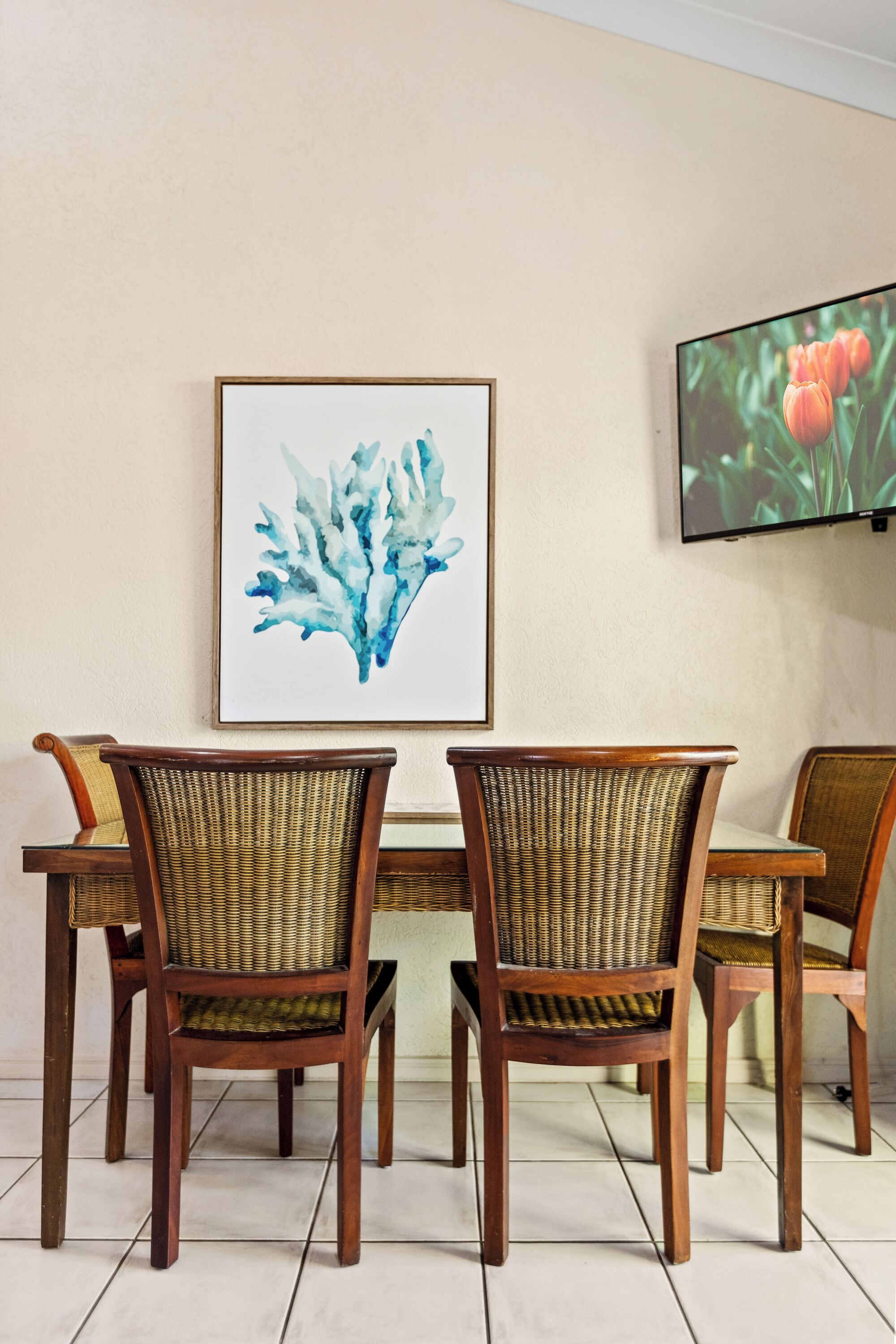 A dining area with a table and chairs, a framed artwork, and a television on the wall.