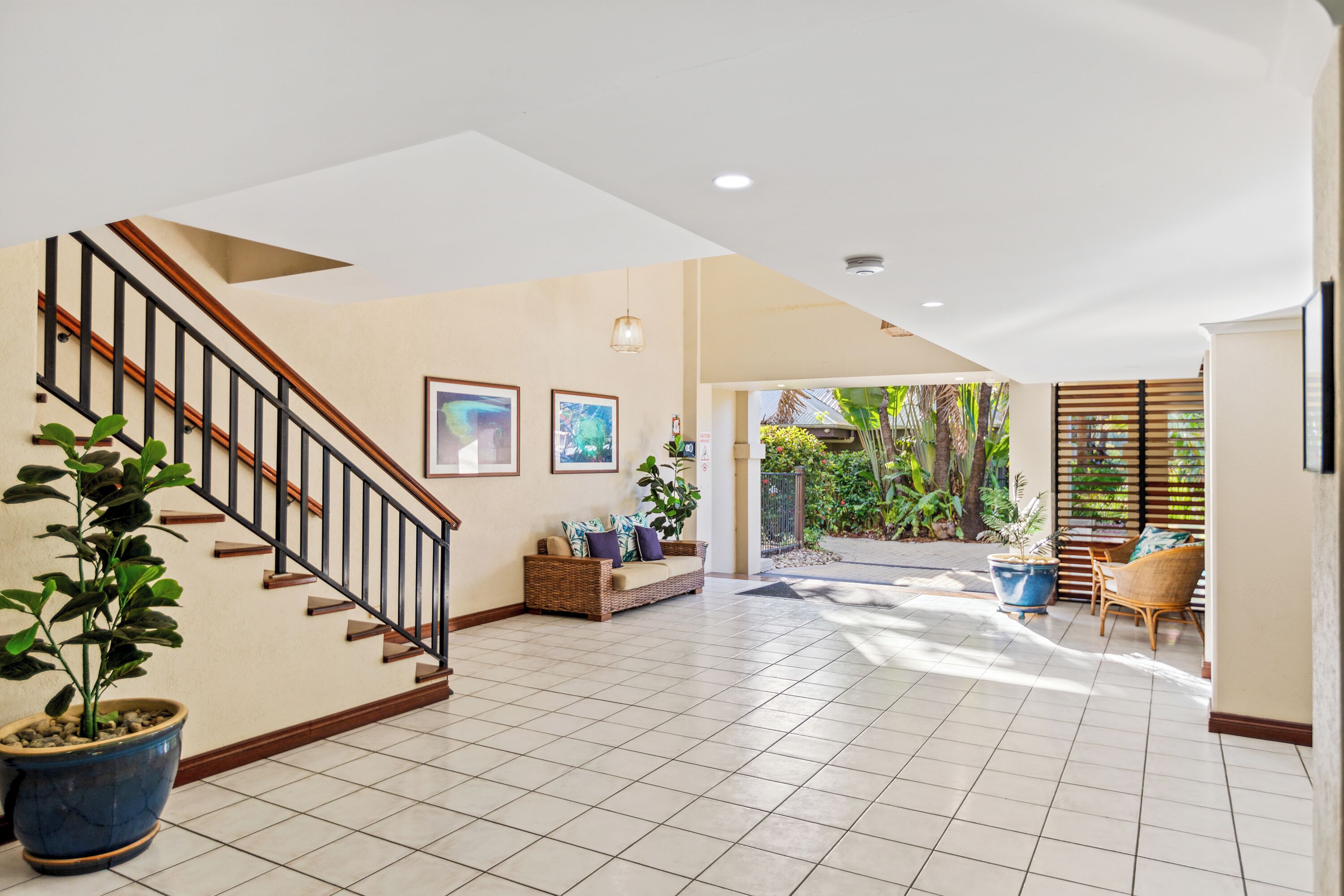 A spacious interior with a staircase, tiled floor, wicker furniture, and potted plants.