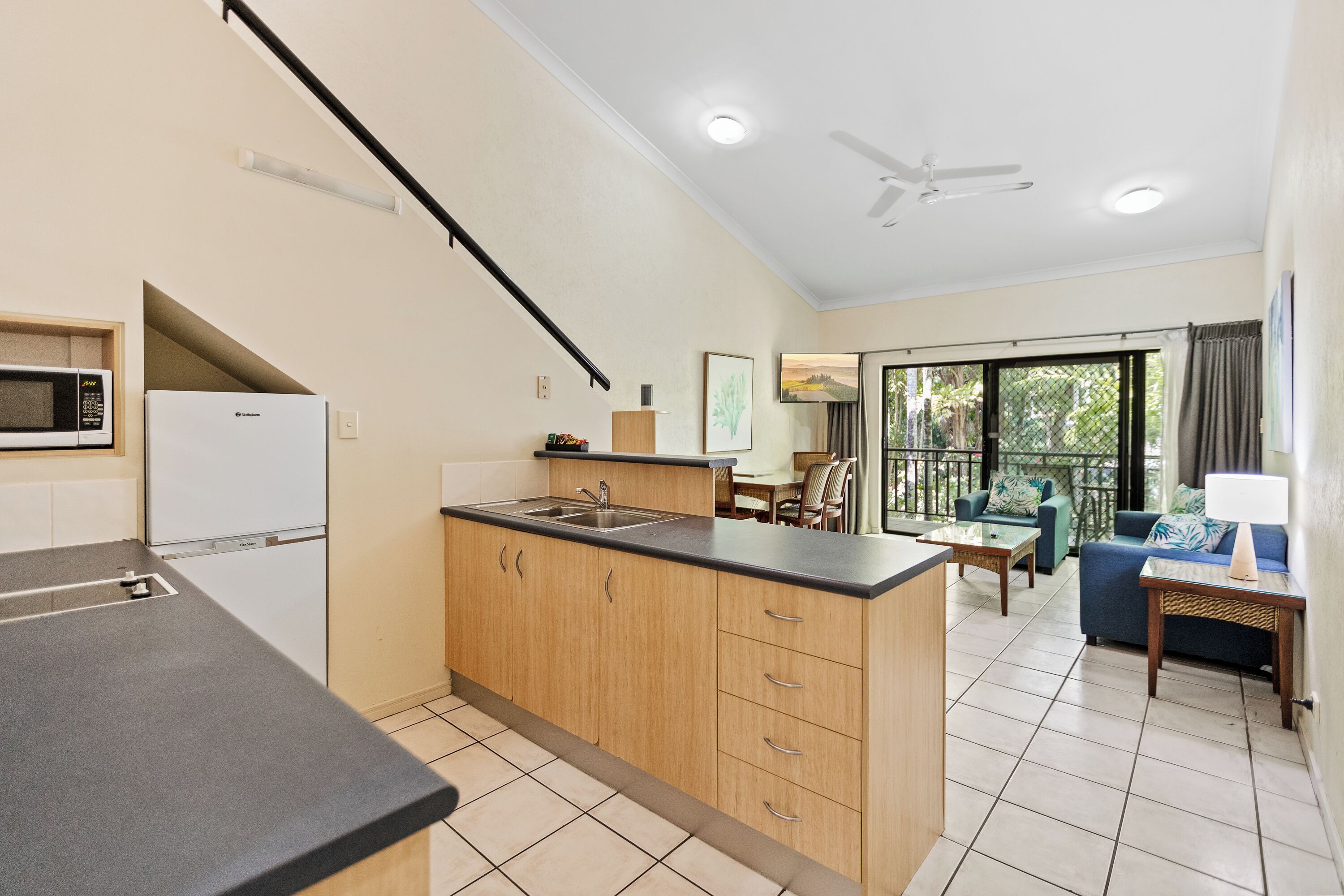 A kitchen with a microwave, refrigerator, and wooden cabinets. There is a dining area with a table and chairs.