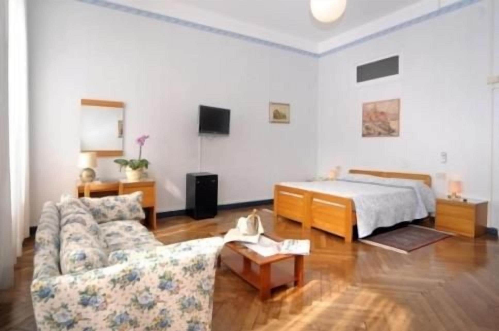 Quarto com cama, sofá, escrivaninha, televisão e espelho.
