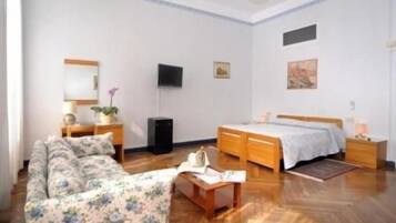 Quarto com cama, sofá, escrivaninha, televisão e espelho.