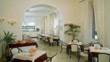 Une salle à manger avec des tables dressées pour le service, un lustre et une vue sur l’extérieur, visible à travers une arche.