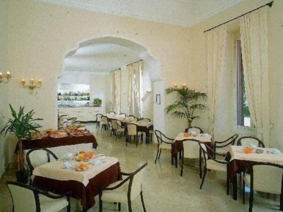Une salle à manger avec des tables dressées pour le service, un lustre et une vue sur l’extérieur, visible à travers une arche.