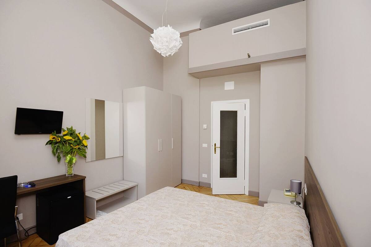 A bedroom with a bed, a desk, a chair, a TV, a mirror, a wardrobe, and a door.