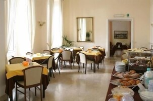 Een eetruimte met meerdere tafels en stoelen, een buffet met diverse gerechten, en een spiegel aan de muur.