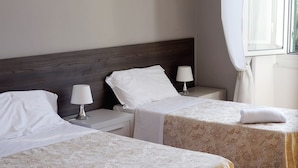 Habitación de hotel con dos camas individuales, cada una con una almohada blanca y una lámpara.