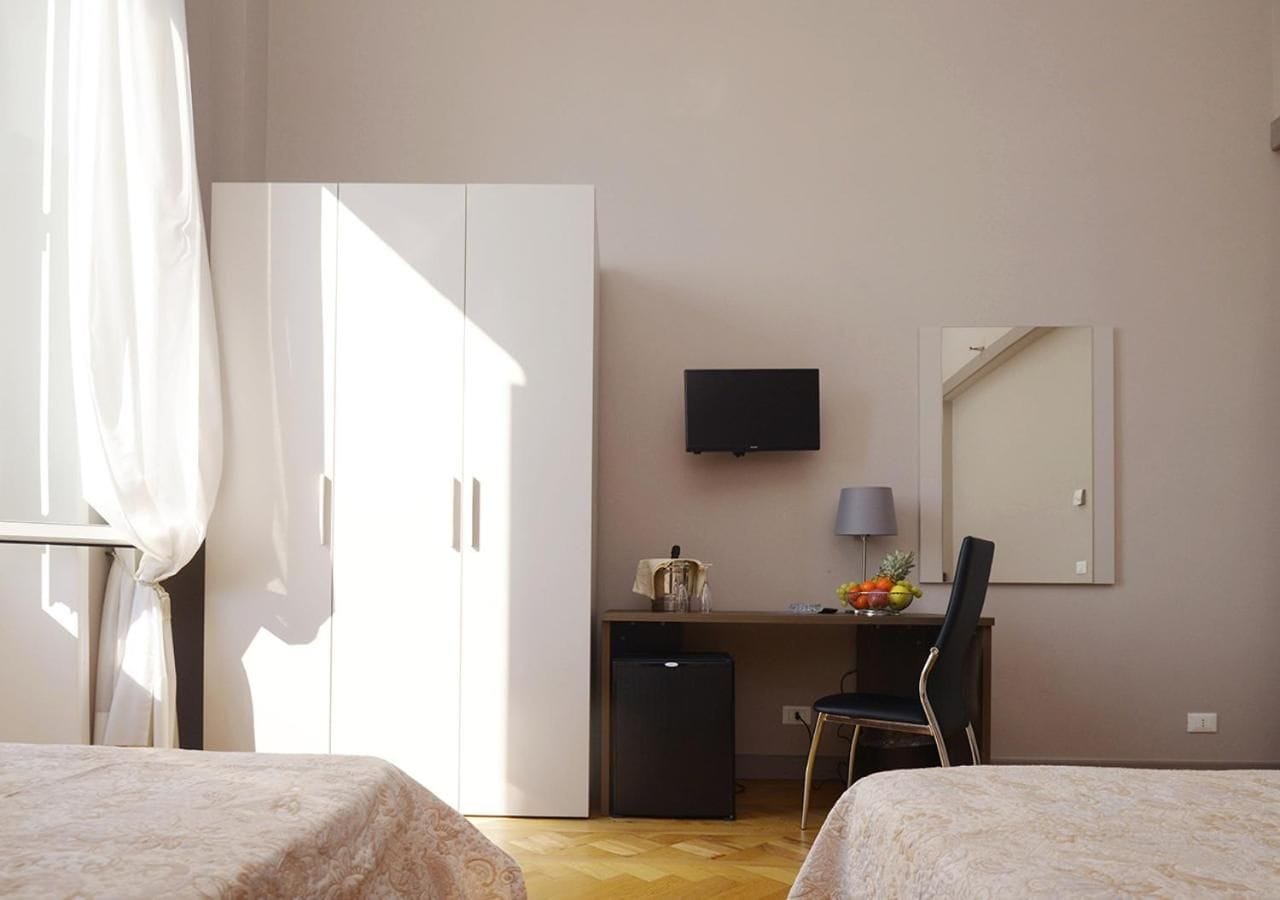 A hotel room with a bed, a desk with a chair, a television, and a small refrigerator.