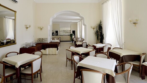 Un comedor de hotel con mesas y sillas, una araña y un bar al fondo.