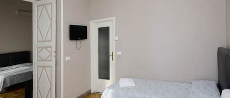 A bedroom with a bed, a desk, and a TV. There is a door leading to another room.