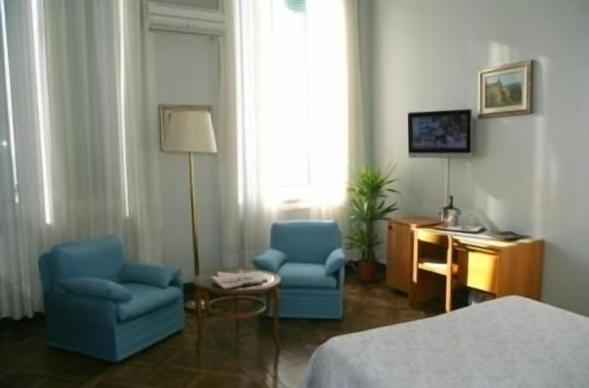 Una habitación de hotel con una cama, dos sillones, un escritorio, un televisor y una ventana con cortinas.