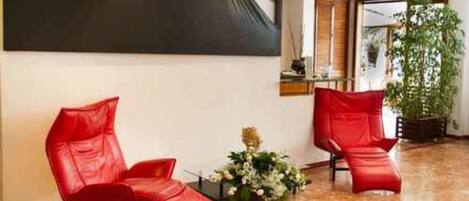 Una habitación con dos sillones de cuero rojo, un cuadro abstracto grande en la pared y una planta en maceta.