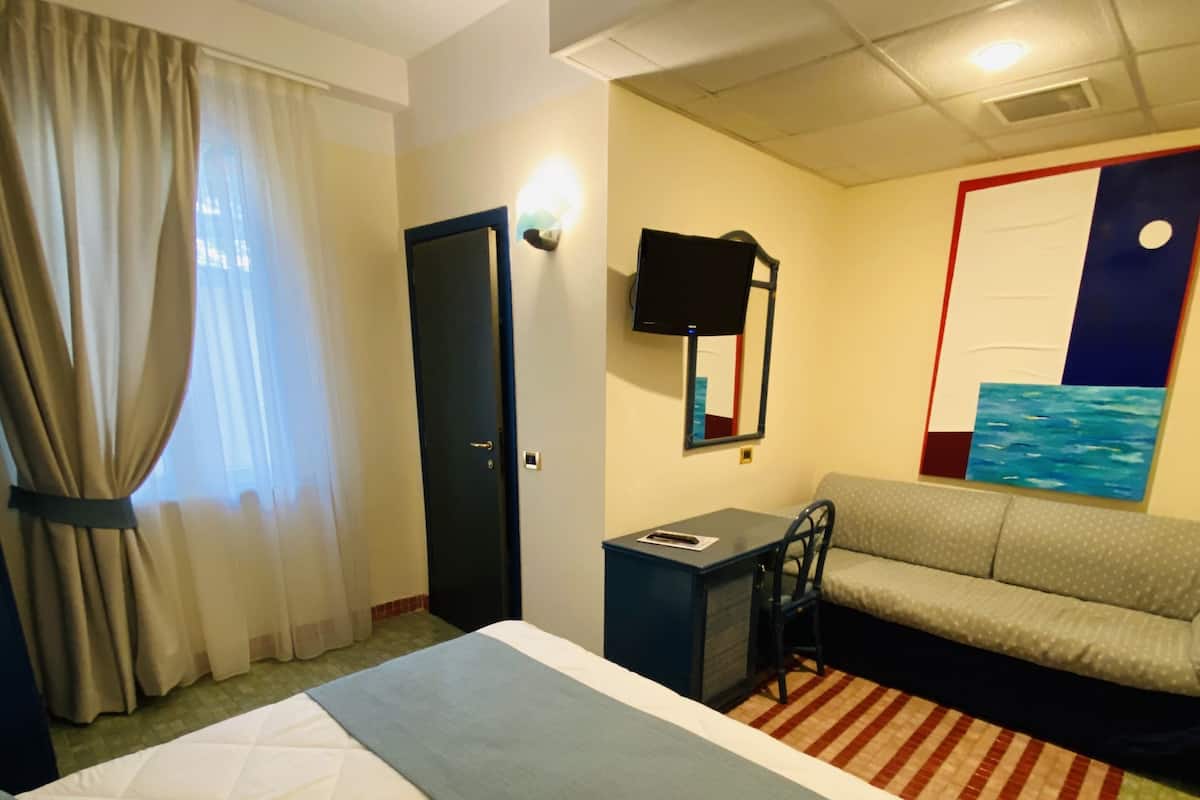 A hotel room with a large bed, a desk, a sofa, and a television.