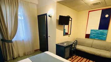 A hotel room with a large bed, a desk, a sofa, and a television.