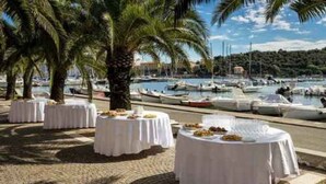 Marina con barcos amarrados, palmeras y mesas redondas con manteles blancos.