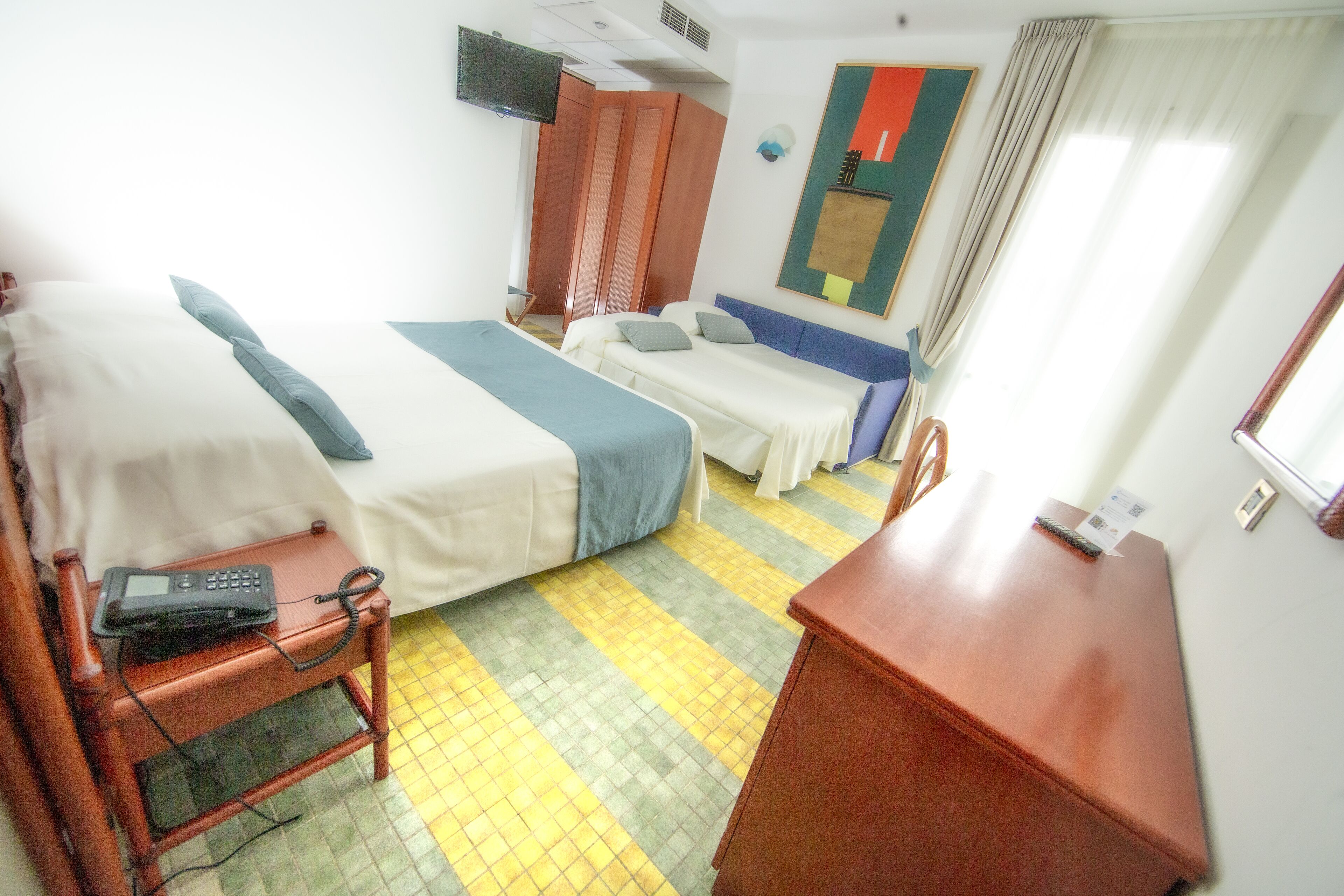 Una habitación de hotel con dos camas, un escritorio con teléfono, una silla y un armario.