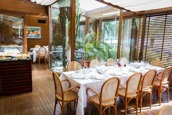 A restaurant with a buffet area, wicker chairs, and a large dining table set for six. - Hotel della Baia (Portovenere)