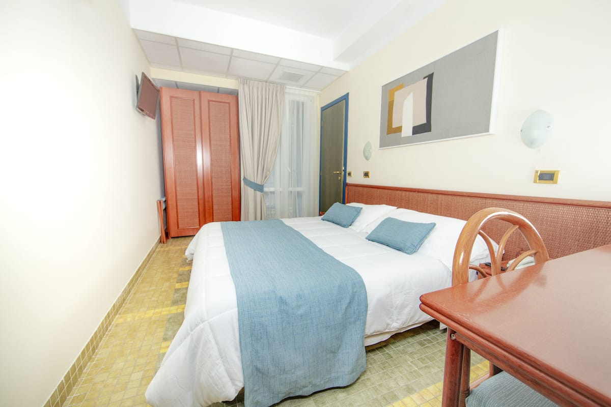 A hotel room with a bed, a wooden chair, a table, a TV, and a door.