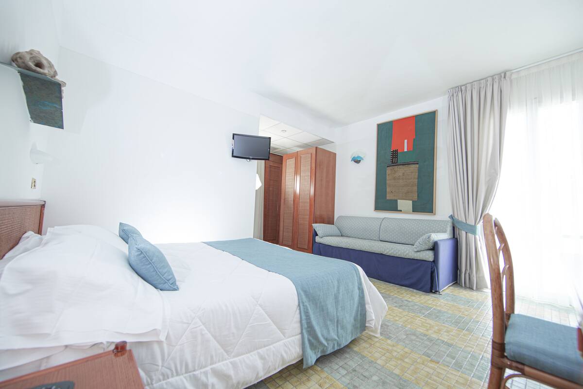 A hotel room with a bed, a sofa, a television, and a chair.