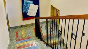 Eine Treppe mit farbenfrohen Fliesenstufen, einem hölzernen Geländer und einem Aushangbrett mit Unterlagen.