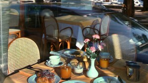 Una mesa dispuesta con alimentos para el desayuno, un jarrón con flores y vista a un puerto deportivo con barcos y palmeras.