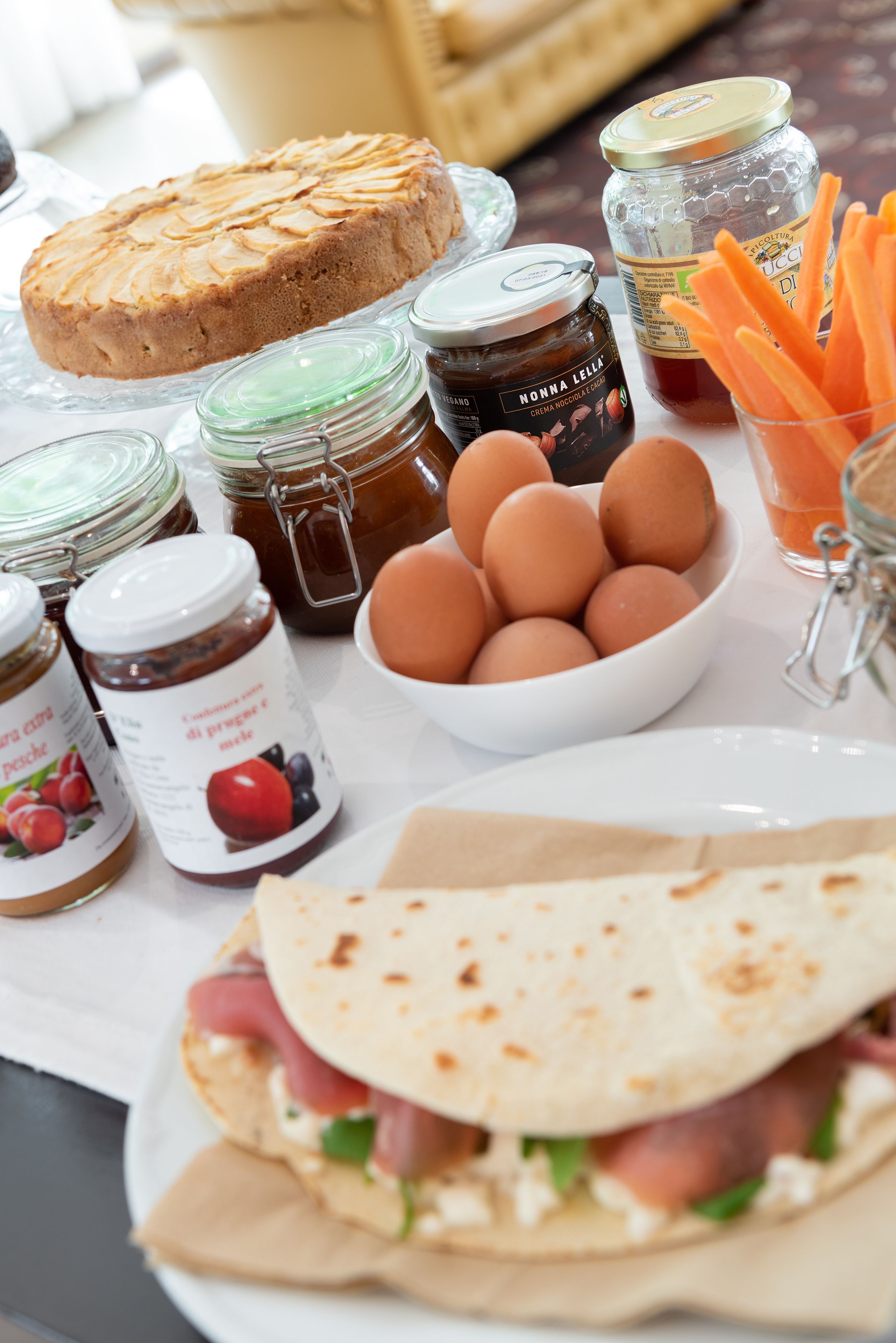 A table with various food items including a cake, eggs, jars of jam, and a sandwich.