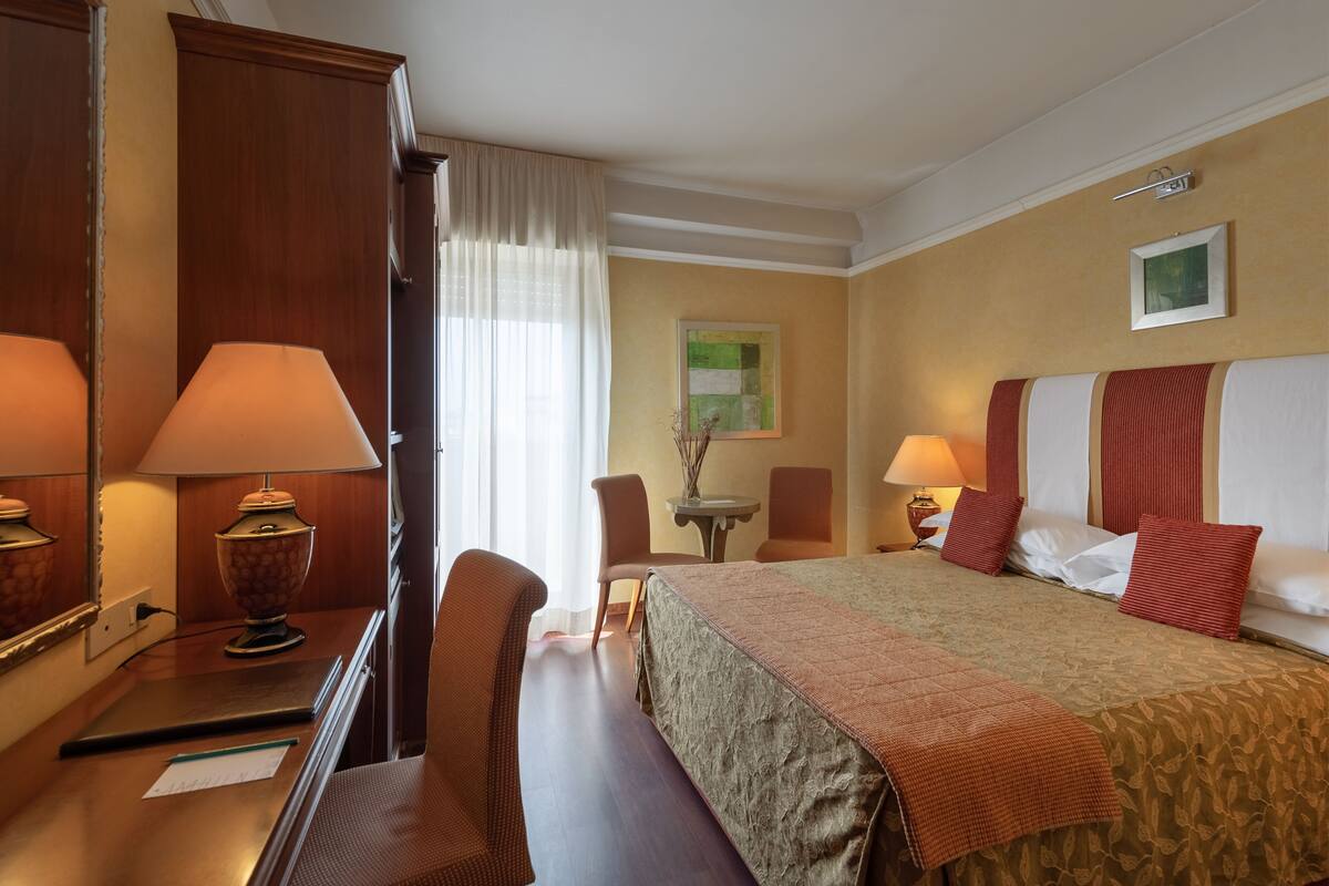 Una habitación de hotel con una cama, dos sillas, un escritorio, una lámpara y una mesita.