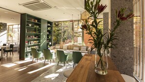 A modern library with green chairs, a wooden table, and a large window with a view of trees. - BIO BOUTIQUE HOTEL XU' (Rimini)