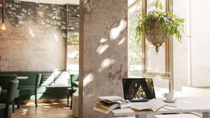 A modern cafe with a green sofa, a white table with a laptop, books, and a hanging plant. - BIO BOUTIQUE HOTEL XU' (Rimini)