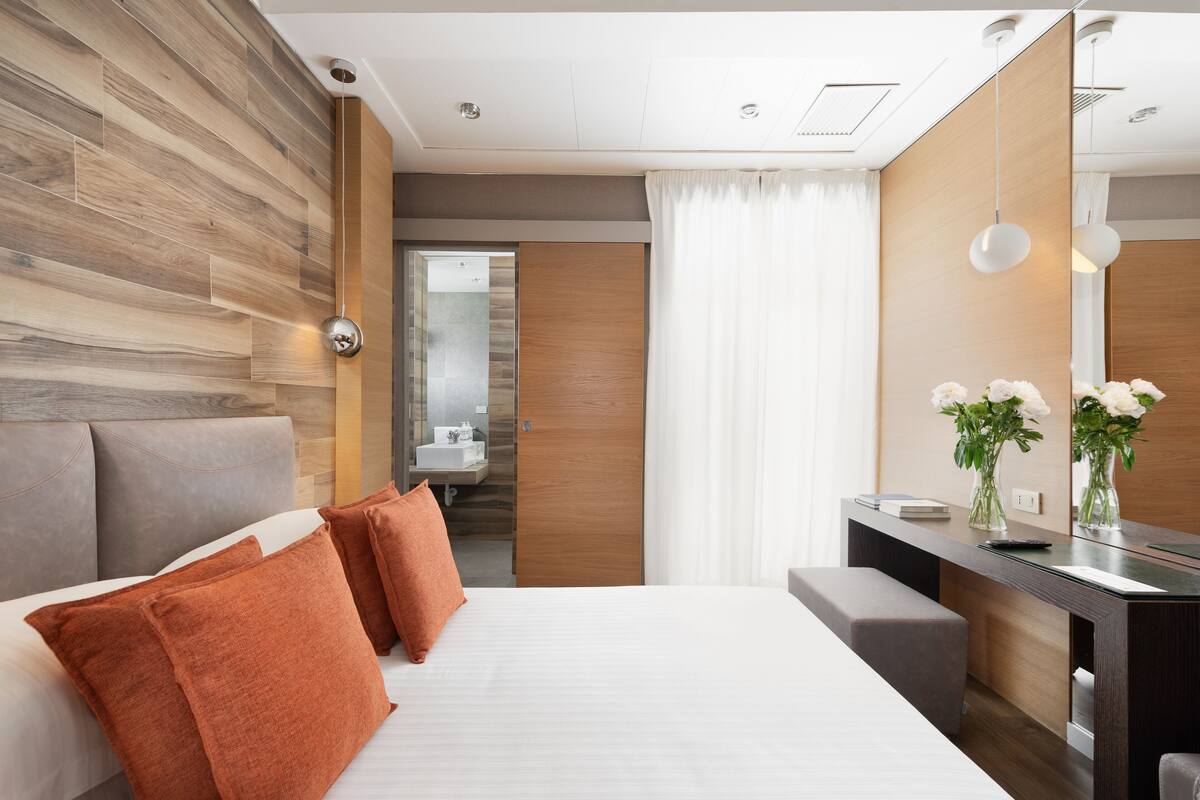 Habitación de hotel moderna con una cama grande, un escritorio y un baño visible a través de una puerta abierta.