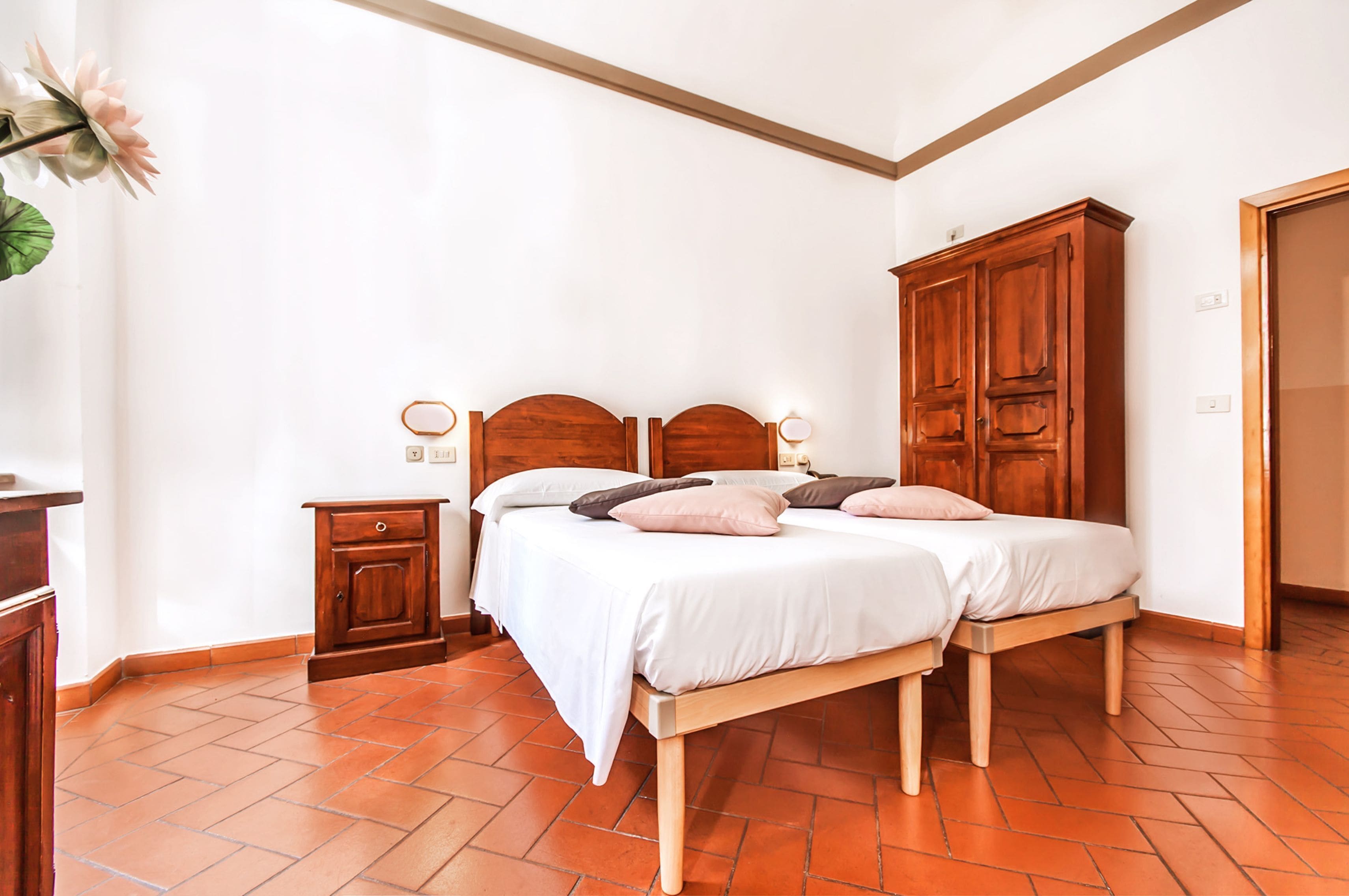 A bedroom with two beds, wooden headboards, a nightstand, and a wardrobe.