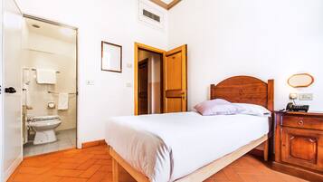 A bedroom with a wooden bed, a bedside table with a lamp, a wooden nightstand, and a bathroom visible through an open door.