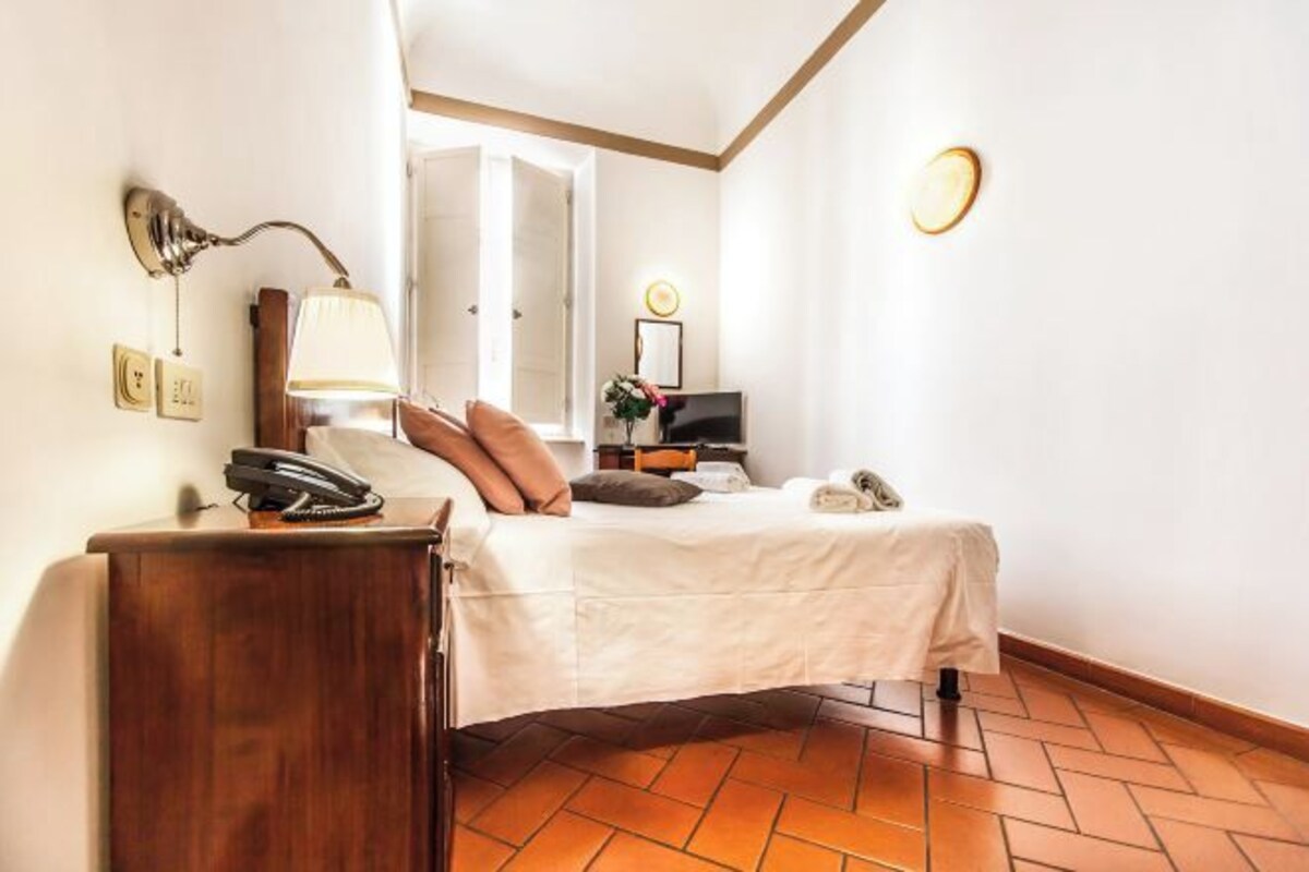 Una habitación de hotel con cama, mesita de noche, lámpara y televisor.