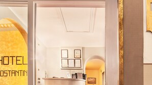 A hotel reception area with a reception desk, framed certificates on the wall, and a tiled floor. - Hotel Costantini (Florence)