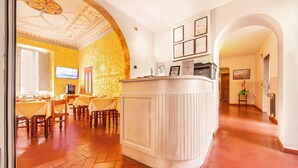 A hotel lobby with a reception desk, a dining area with tables and chairs, and a tiled floor. - Hotel Costantini (Florence)