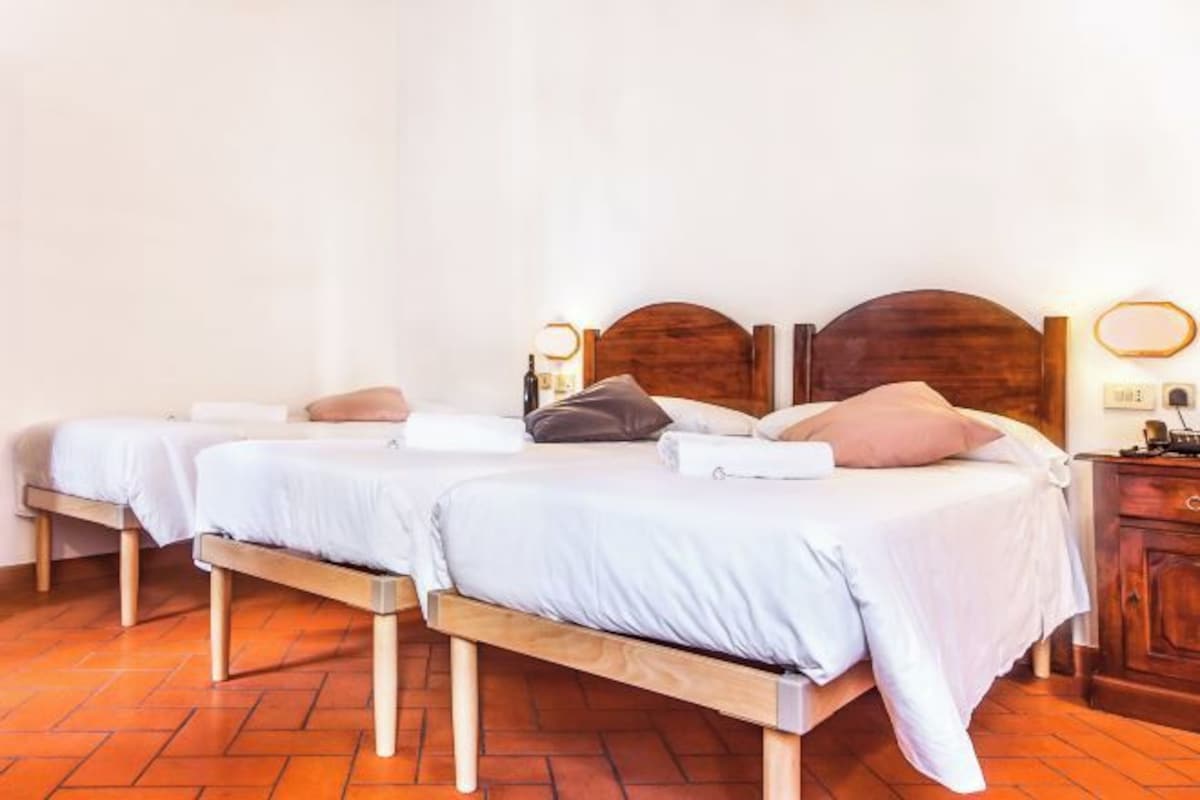 Una habitación de hotel con dos camas individuales, cabeceros de madera, una mesita de noche de madera y una lámpara de pared, además de un suelo con diseño de espiga.