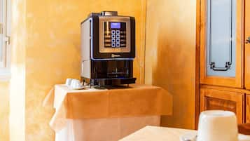 A hotel room with a coffee machine, a television displaying a scenic view, and a dining table set with a cup and a knife.